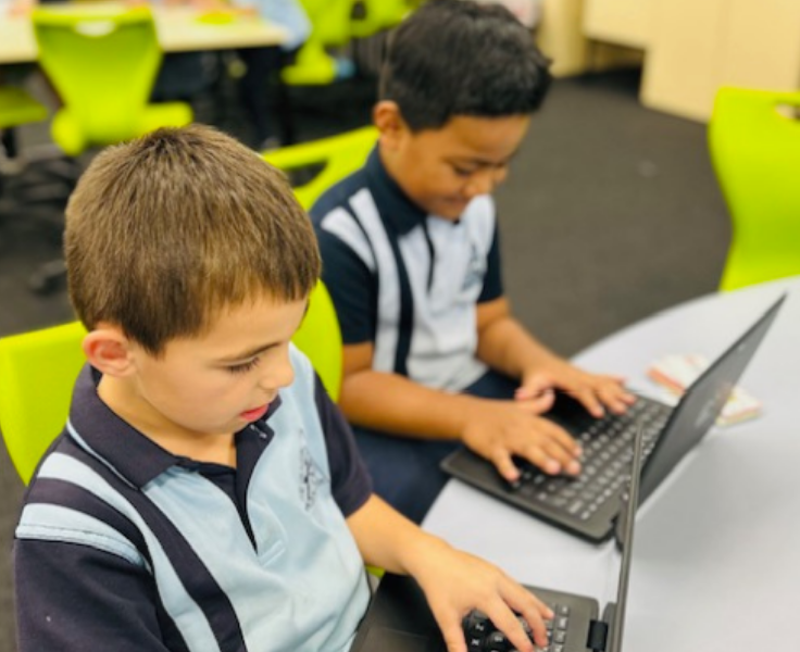 Two students sitting at a table working hard on laptios.