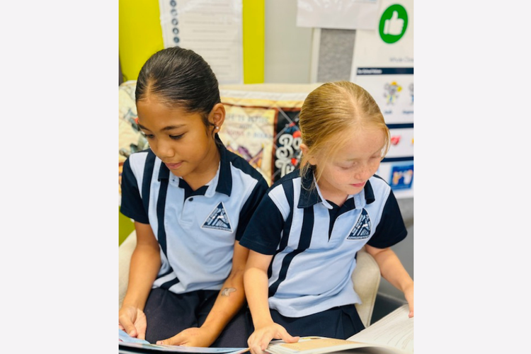 Photo of two students in the library reading a book each.