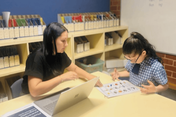 A Teacher sitting with a student help with her learning needs.