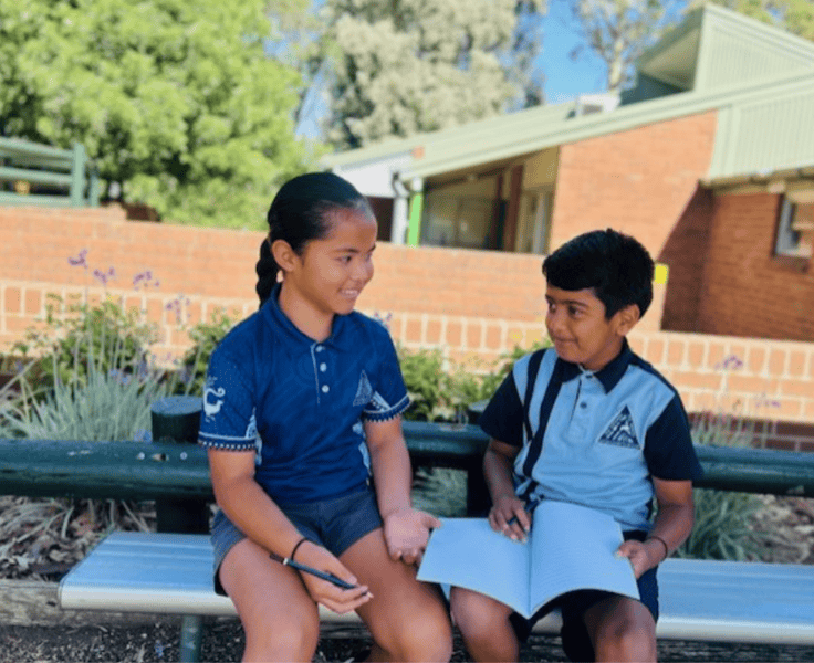 Two students sitting on a seat in the playground going through their debating topic and making notes.